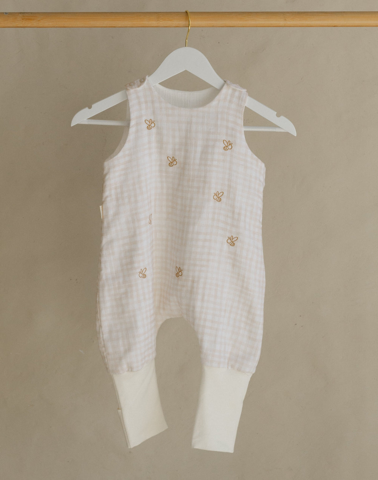White baby romper hanging on a wooden rack against a beige background