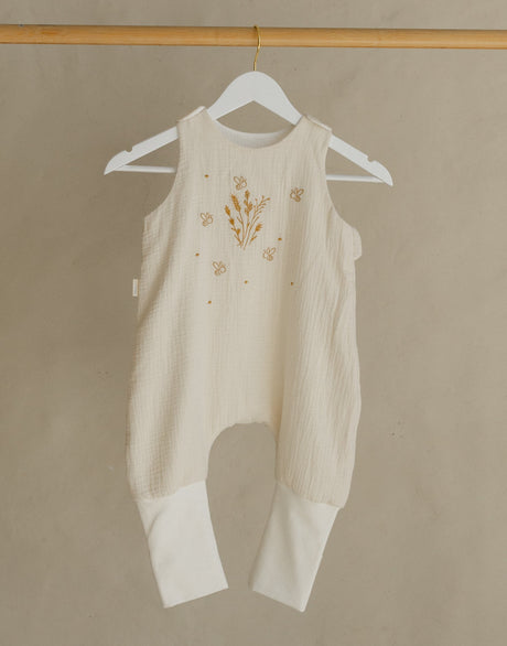 White baby romper on a hanger attached to a wooden rack against a beige wall.