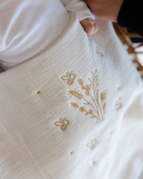 Baby lying on a white blanket with floral embroidery, held by a person.