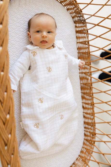 Baby in a white outfit with gold accents lying in a wicker crib.