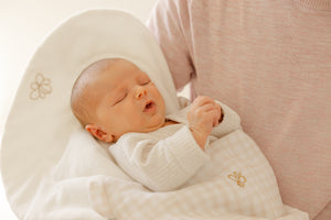 Newborn baby wrapped in a white blanket with a gold flower design, lying on a white pillow.