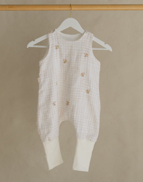 White baby romper hanging on a wooden rack against a beige background