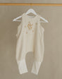 White baby romper on a hanger attached to a wooden rack against a beige wall.