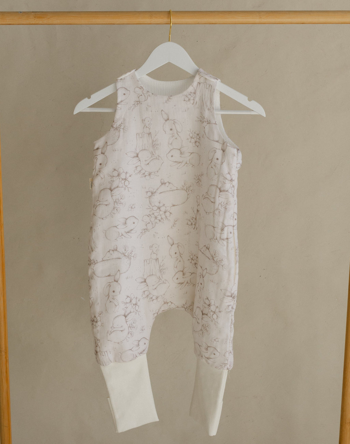 Gold clothing rack with a white baby romper on a beige background