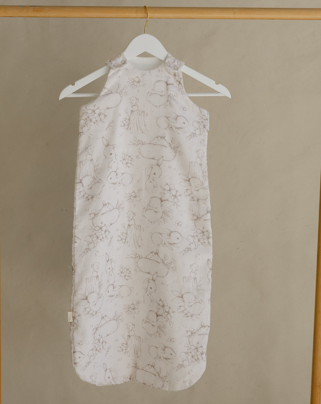 Light-colored dress with floral pattern hanging on a wooden rack against a beige wall.