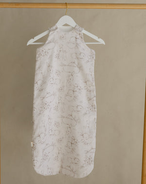 Light-colored dress with floral pattern hanging on a wooden rack against a beige wall.