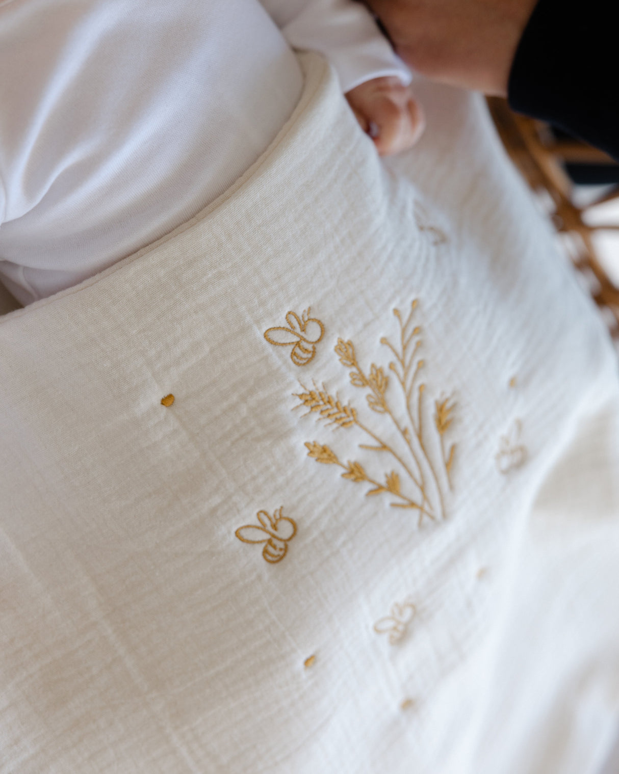 Baby lying on a white blanket with floral embroidery, held by a person.