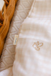 Close-up of a textured beige fabric with a small embroidered bee design and a visible brand tag.